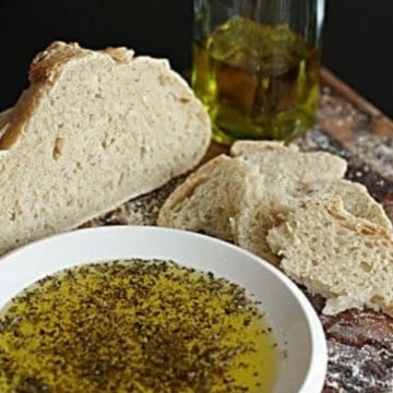 italian dipping oil for bread on a white ceramic plate next to a loaf of sourdough bread