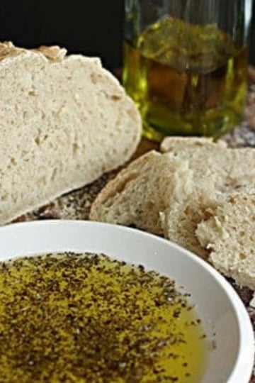 italian dipping oil for bread on a white ceramic plate next to a loaf of sourdough bread