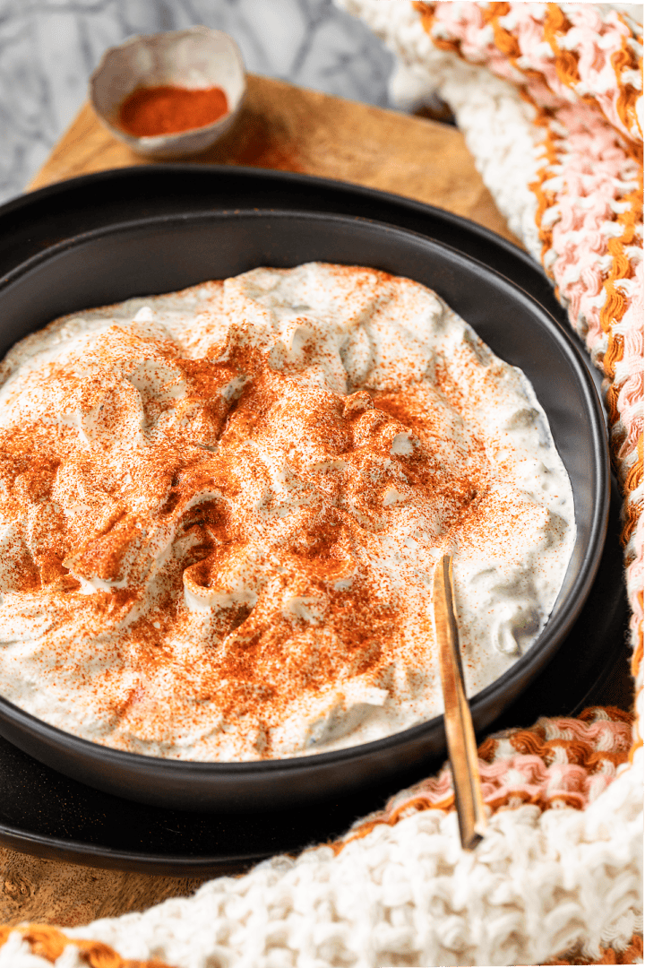 creamy cucumber salad with sour cream sprinkled with Hungarian paprika in a black serving bowl with a colorful dish towel