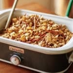 chex mix in a slow cooker with a wooden spoon