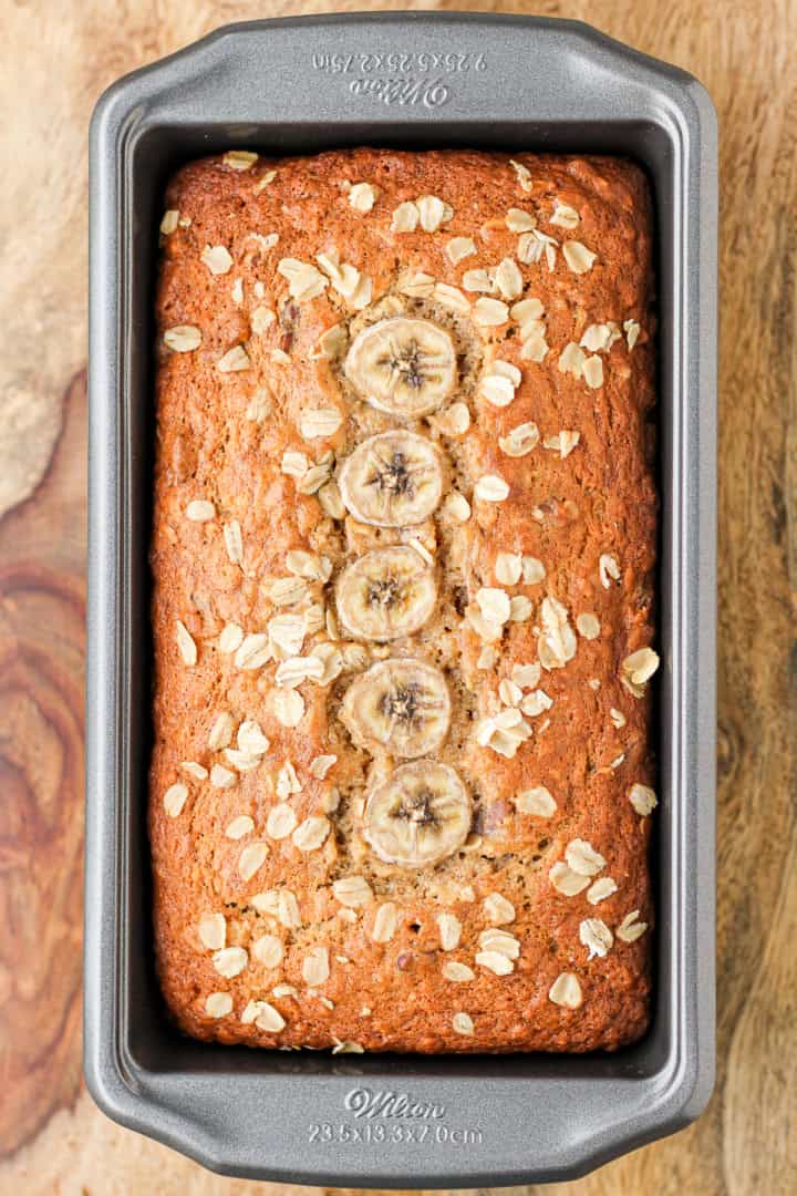 banana quick bread topped with sliced bananas in an aluminum loaf pan