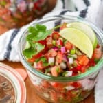 raw salsa recipe in a glass jar with lime wedges