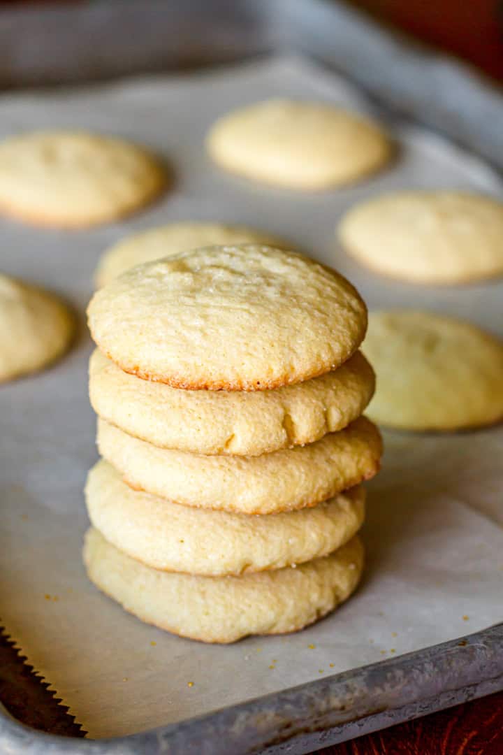 drop sugar cookies stacked on a rimmed baking sheet lined with parchment paper