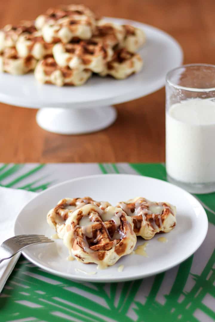 cinnamon roll waffles drizzled with cream cheese glaze syrup on a white ceramic plate with a fork