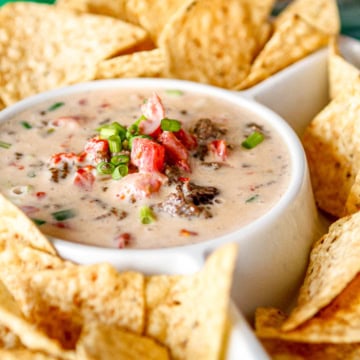 velveeta queso with ground beef garnished with chopped green onions surrounded by tortilla chips