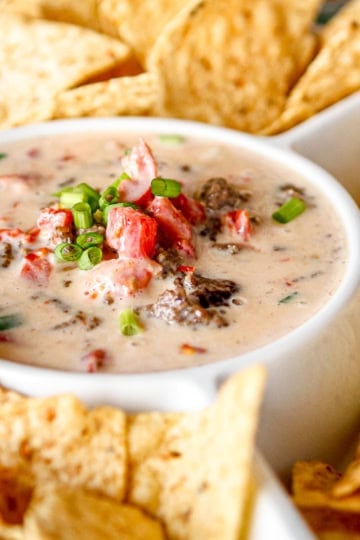 velveeta queso with ground beef garnished with chopped green onions surrounded by tortilla chips