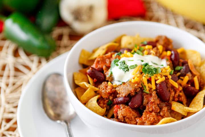 sausage chili recipe in a bowl topped with fritos and sour cream