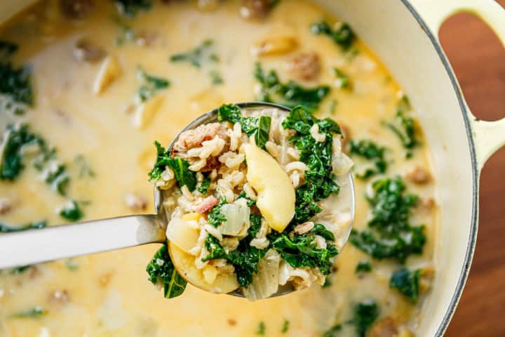 zuppa toscana Italian sausage soup in a ladle over a Dutch oven