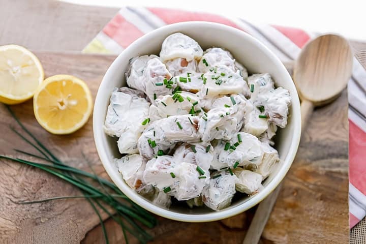 creamy red skin potato salad in a ceramic bowl with a wooden spoon