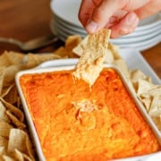 male hand scooping buffalo chicken dip up with a tortilla chip