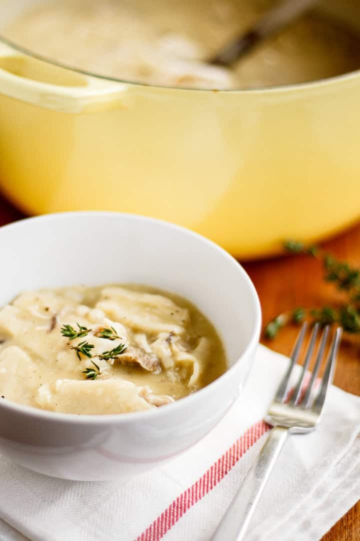 rotisserie chicken and dumplings in a white ceramic bowl garnished with fresh thyme