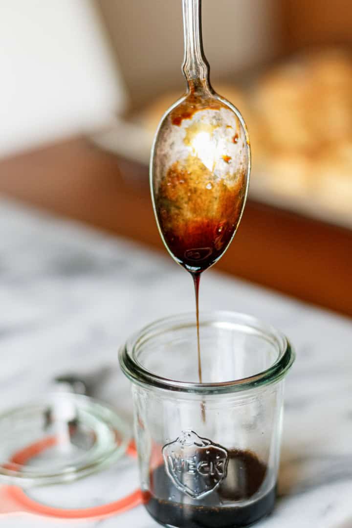 thick balsamic vinegar reduction being drizzled off a silver spoon into a glass weck jar