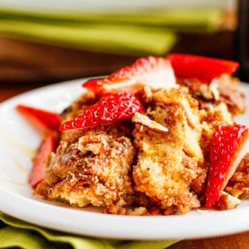 hawaiian roll french toast bake scooped on a ceramic plate garnished with fresh strawberries