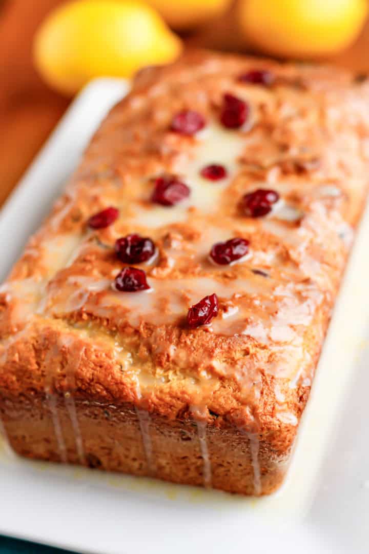loaf of lemon bread topped with lemon glaze and dried cranberries on a white ceramic platter