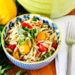 lemon orzo pasta salad in a yellow-rimmed blue ceramic bowl garnished with fresh Italian parsley