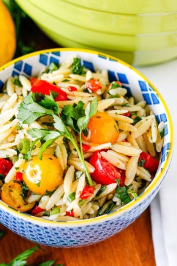 lemon orzo pasta salad in a yellow-rimmed blue ceramic bowl garnished with fresh Italian parsley