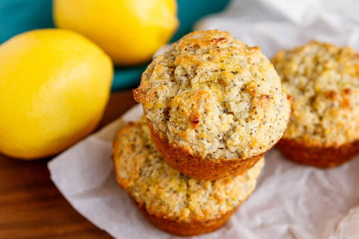 lemon poppy seed muffins stacked on a piece of parchment paper with fresh lemons