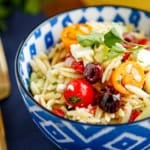 greek orzo salad with feta and kalamata olives in a blue ceramic bowl garnished with fresh parsley