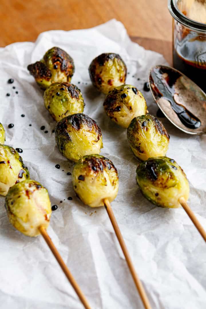 grilled brussel sprouts on crinkled white parchment paper with balsamic reduction drizzled over top