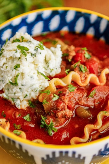 easy lasagna soup recipe in a blue and white bowl garnished with a creamy ricotta Parmesan topping and parsley