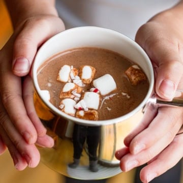 child's hands holding mug of homemade hot chocolate mix topped with marshmallows and candy cane pieces