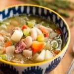 ham and bean soup recipe made with leftover ham bone in a blue and white patterned ceramic bowl with a yellow rim
