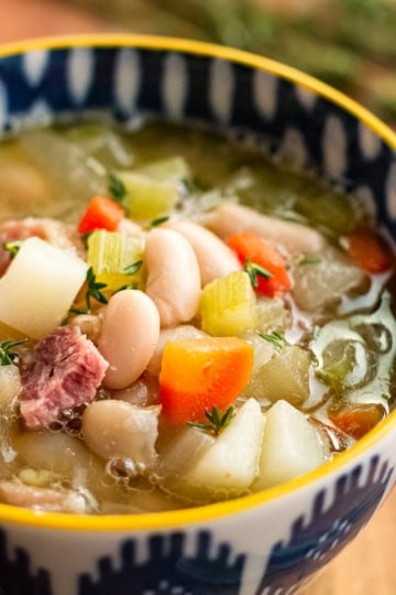 ham and bean soup recipe made with leftover ham bone in a blue and white patterned ceramic bowl with a yellow rim