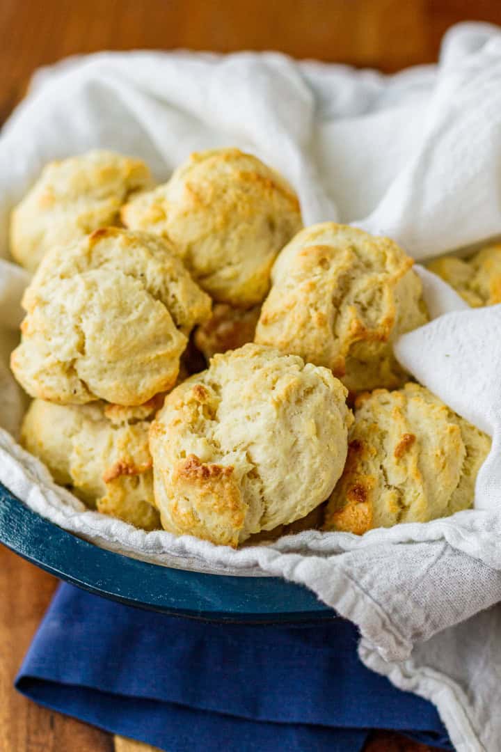 cream biscuits in a wood bowl with a blue rim lined with a white towel