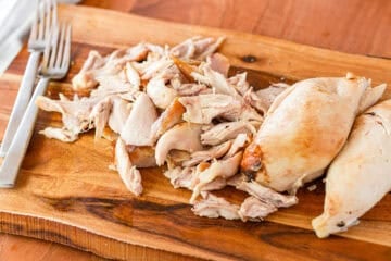 cut rotisserie chicken on a wood cutting board with two forks