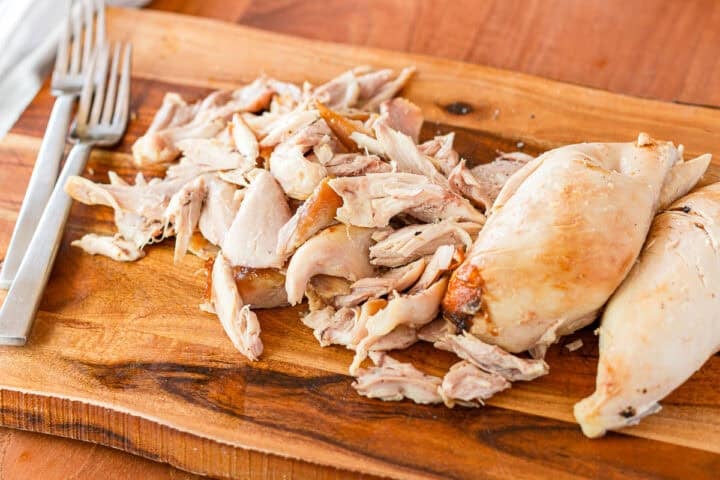 cut rotisserie chicken on a wood cutting board with two forks