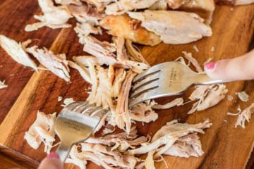 shredded and pulled rotisserie chicken using 2 forks on a wood cutting board