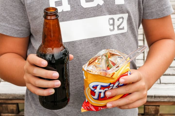 boy holding a walking taco bag with a plastic fork and a root beer