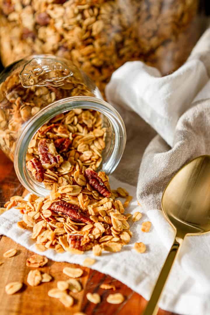 oat and honey granola spilling out of a glass jar with a gold spoon