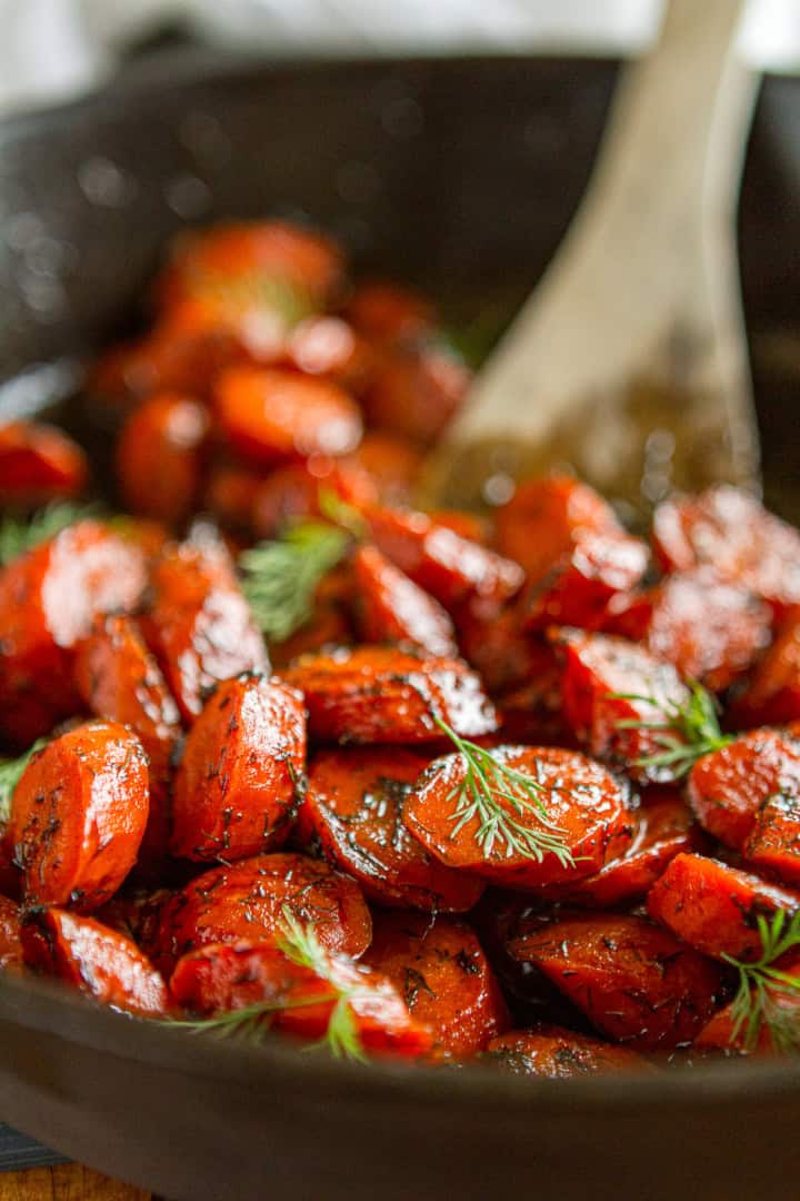 brown butter honey roasted carrots garnished with fresh dill in a cast iron pan