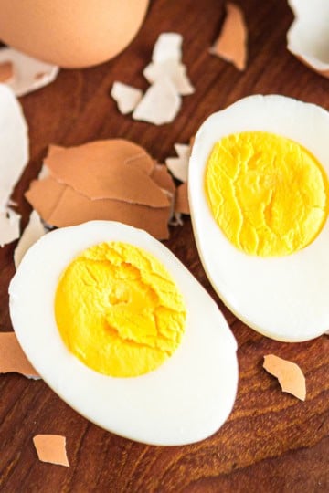 peeled hard boiled eggs with shell fragments on a wooden table