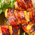 bacon wrapped corn on the cob piled up on brown parchment paper