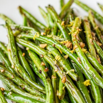 sautéed green beans with garlic garnished with lemon zest on a white ceramic plate