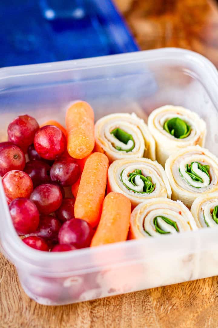 hummus turkey pinwheels in a plastic container carrots and red grapes