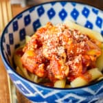 ground chicken penne pasta garnished with parmesan cheese in a blue and white ceramic bowl