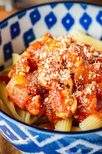 ground chicken penne pasta garnished with parmesan cheese in a blue and white ceramic bowl