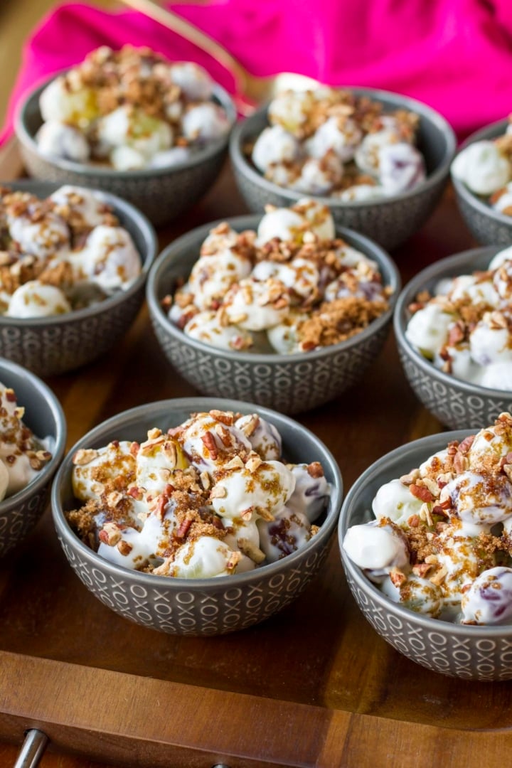 bowls of grape salad with cream cheese topped with brown sugar and toasted pecans on a wooden tray