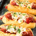 crockpot meatball subs recipe topped with melted mozzarella cheese and chopped fresh parsley on a baking sheet