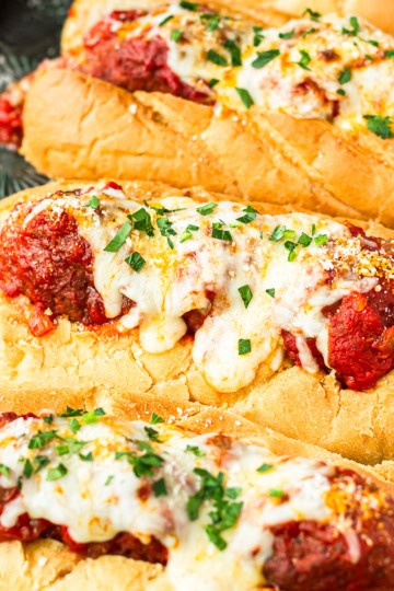 crockpot meatball subs recipe topped with melted mozzarella cheese and chopped fresh parsley on a baking sheet