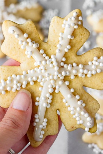 hand holding a snowflake sugar cookie piped with easy royal icing recipe and sprinkled with sugar pearls