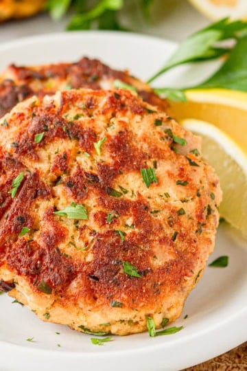 crispy fried tuna patties on white parchment paper with fresh Italian parsley and lemon wedges