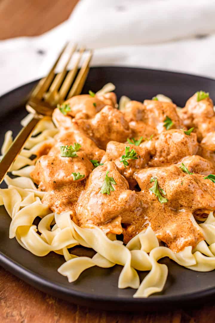 chicken paprikash over egg noodles on a black plate with a gold fork