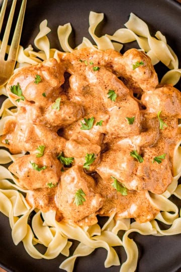chicken paprikas recipe over egg noodles on a black ceramic plate