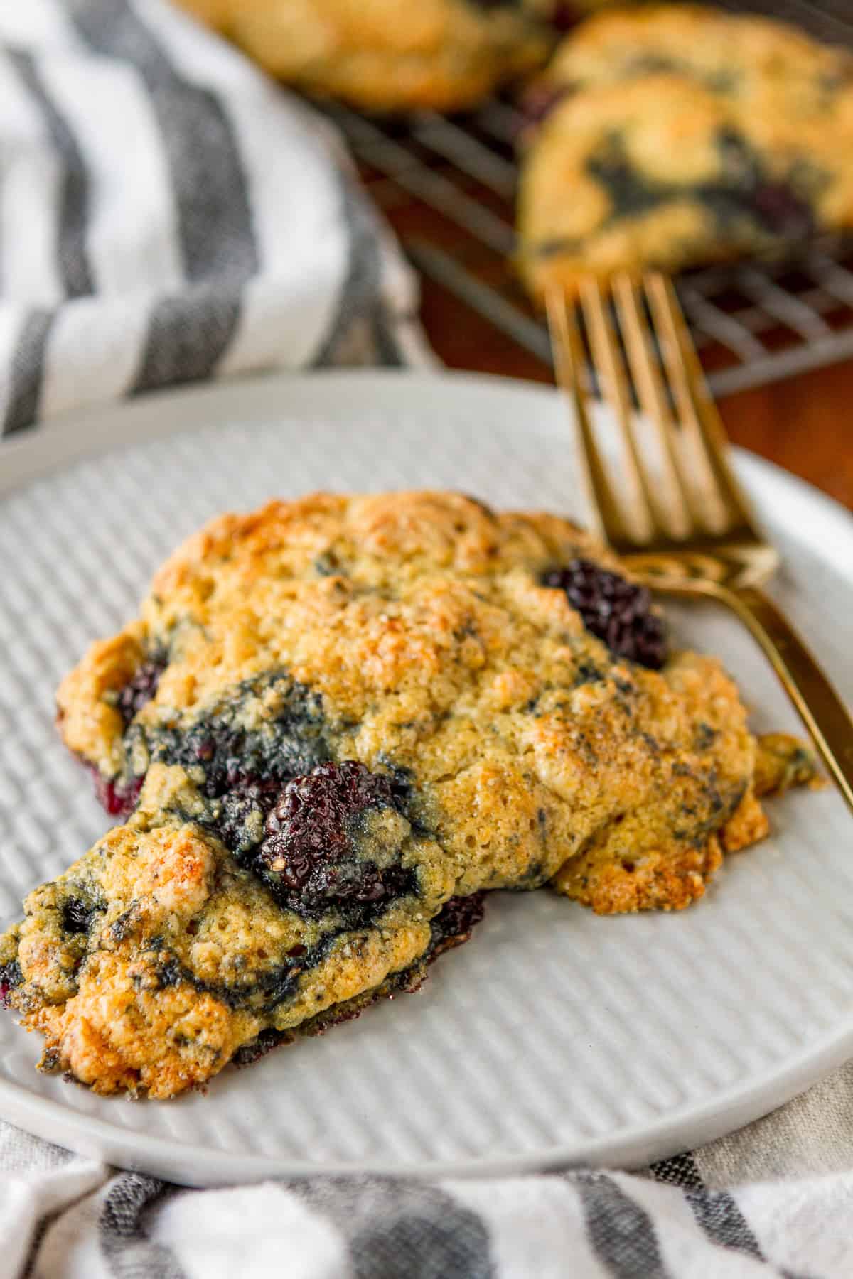 tender and buttery blackberry scone on a white textured plate with a gold fork