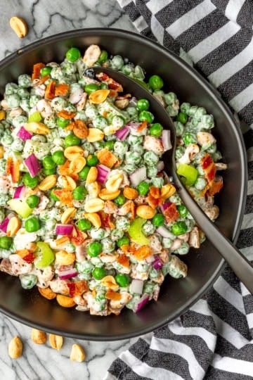 pea salad recipe with bacon and peanuts in a black bowl with a black spoon