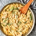 chicken spinach alfredo pasta recipe in a skillet with a black and white striped towel wrapped around the handle